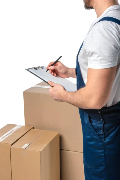 Vue partielle du déménageur en écriture uniforme dans un presse-papiers près de boîtes en carton isolées sur du blanc — Photo de stock