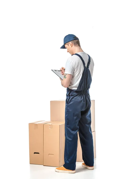 Vista trasera del motor en escritura uniforme en portapapeles cerca de cajas de cartón aisladas en blanco — Stock Photo