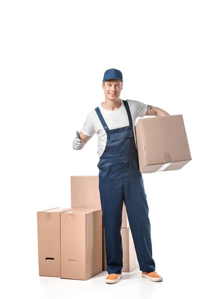 Guapo mover en uniforme llevando caja de cartón y mostrando el pulgar hacia arriba signo aislado en blanco - foto de stock