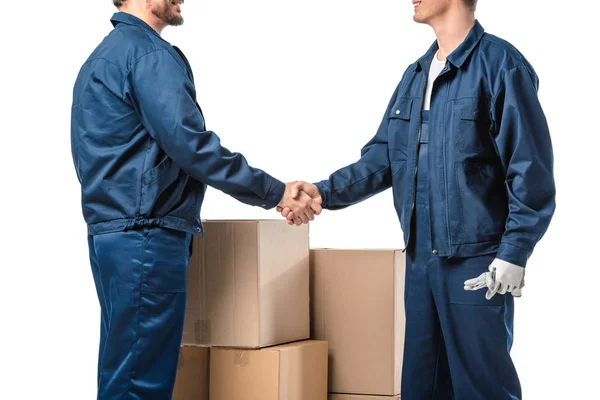 Cropped view of two movers in uniform shaking hands near cardboard boxes isolated on white — Stock Photo