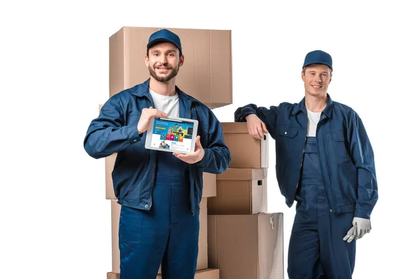 Two smiling movers with cardboard boxes presenting digital tablet with amazon app on screen isolated on white — Stock Photo