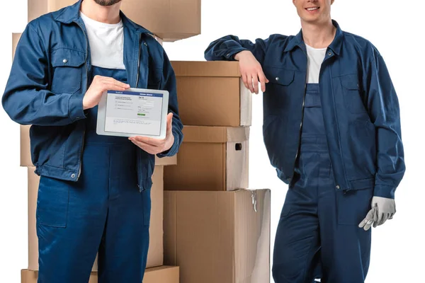 Cropped view of two movers with cardboard boxes presenting digital tablet with facebook app on screen isolated on white — Stock Photo