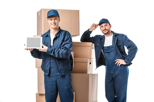 Two movers with cardboard boxes looking at camera and presenting digital tablet with blank screen isolated on white — Stock Photo