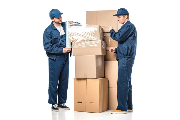 Two movers wrapping cardboard boxes with roll of stretch film on white — Stock Photo