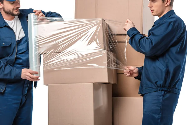 Deux déménageurs enveloppant boîtes en carton avec rouleau de film étirable isolé sur blanc — Photo de stock