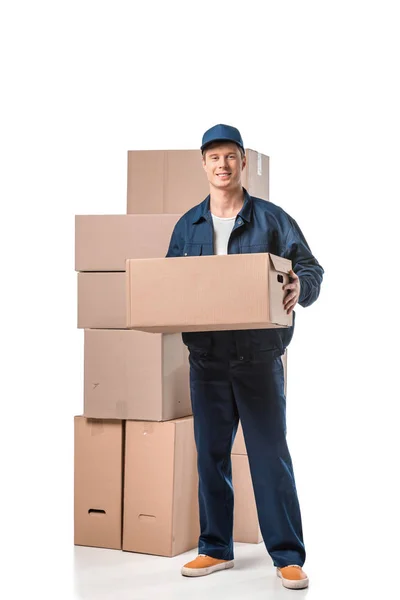 Bonito mover no uniforme transportando caixa de papelão e olhando para a câmera isolada no branco — Fotografia de Stock