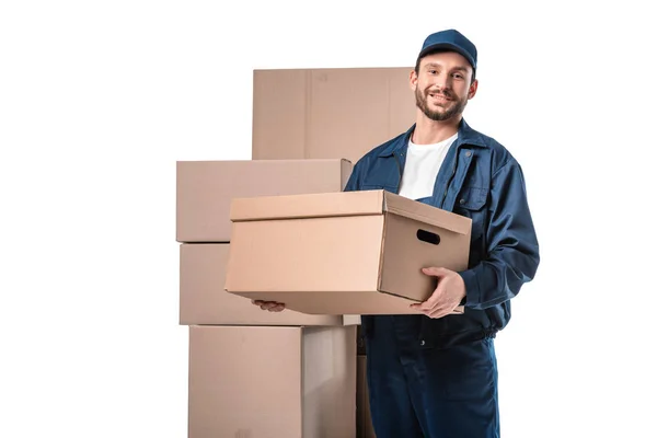 Smiling handsome mover in uniform carrying cardboard box and looking at camera isolated on white with copy space — Stock Photo