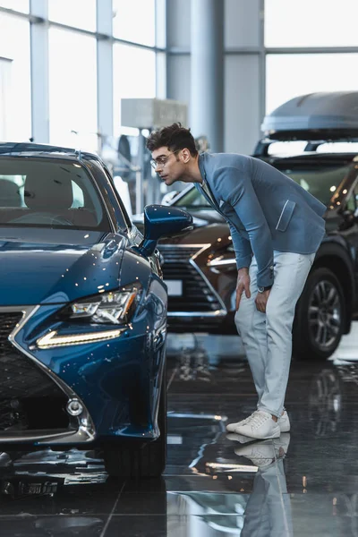 Handsome stylish man in glasses standing near auto in car showroom — Stock Photo