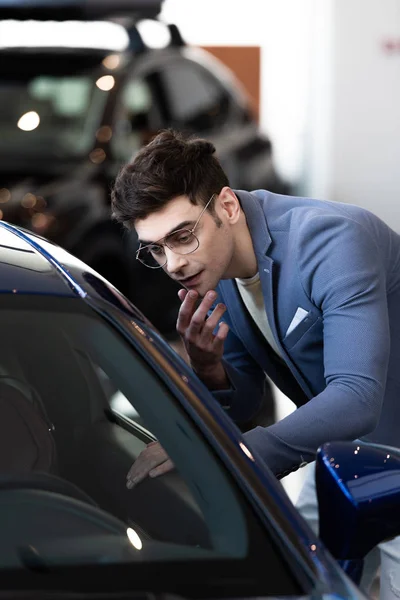Pensive customer in glasses looking at automobile while standing in car showroom — Stock Photo