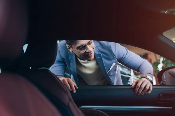 Enfoque selectivo del hombre alegre en gafas mirando en el coche - foto de stock