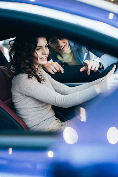 Foyer sélectif de femme heureuse assise dans l'automobile près de l'homme joyeux pointant du doigt — Photo de stock