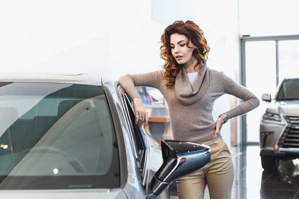 Bela mulher encaracolado de pé perto do veículo no showroom carro — Fotografia de Stock