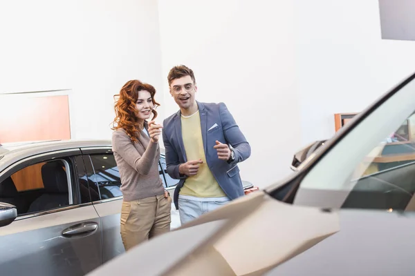 Enfoque selectivo de la mujer rizada alegre y hombre feliz señalando con los dedos en el coche - foto de stock