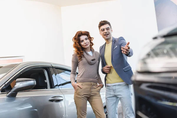 Foyer sélectif de la femme bouclée debout avec la main dans la poche près de l'homme pointant du doigt à la voiture — Photo de stock