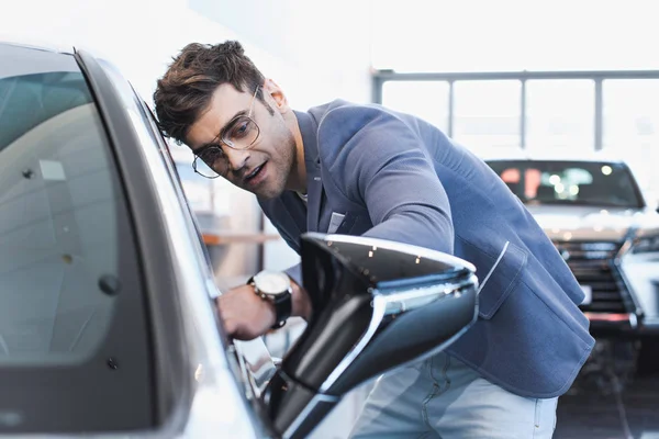 Exitoso hombre con estilo en gafas de pie cerca de auto en sala de exposición de coches - foto de stock