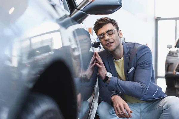 Selektiver Fokus des glücklichen, stilvollen Mannes mit Brille, der in der Nähe von Auto im Autohaus lächelt — Stockfoto