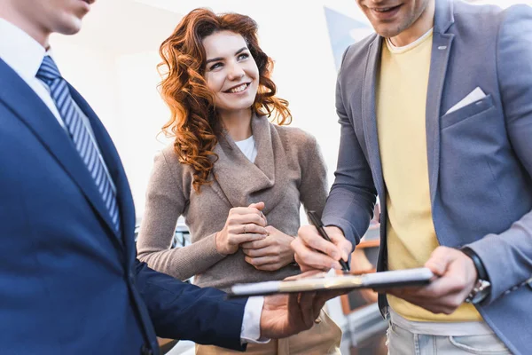 Cropped view of man signing contract with car dealer near cheerful woman — Stock Photo