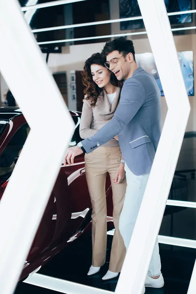 Happy man smiling near curly girl while looking at red automobile — Stock Photo