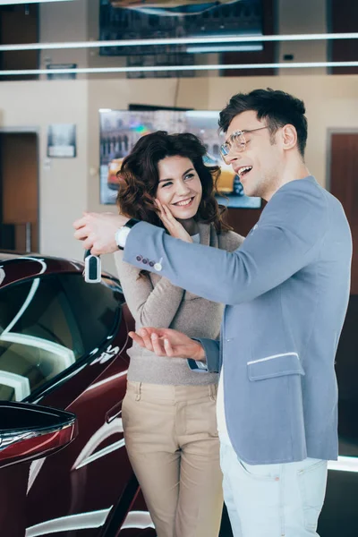 Mujer feliz mirando hombre guapo sosteniendo llaves cerca de automóvil rojo - foto de stock