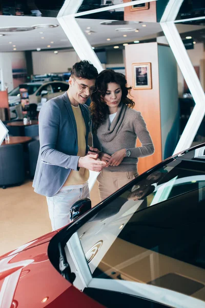 Attractive woman standing with handsome man pointing with finger at red automobile — Stock Photo