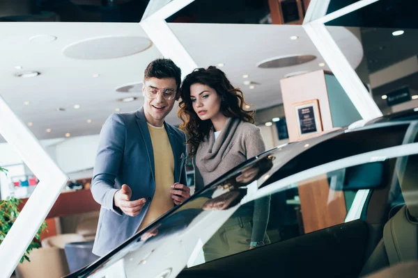 Cheerful man pointing with finger at red automobile near attractive woman — Stock Photo