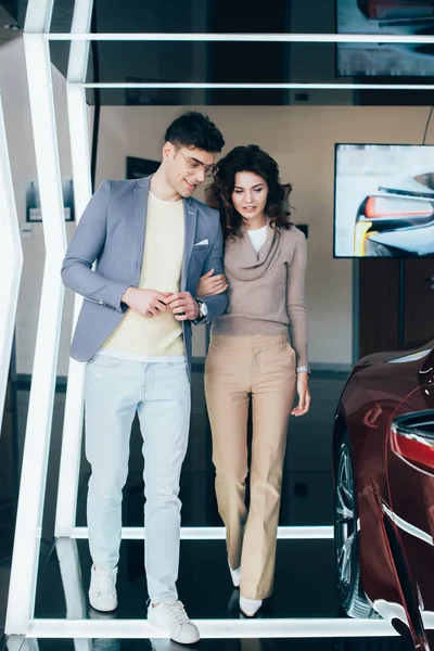 Hombre elegante caminando con chica rizada cerca de automóvil rojo - foto de stock