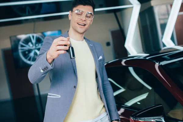 Foco seletivo do homem alegre em óculos segurando chaves enquanto está perto do automóvel vermelho — Fotografia de Stock