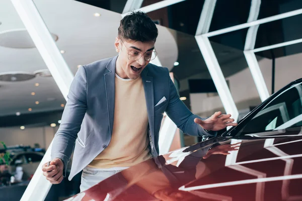 Selektiver Fokus des aufgeregten, stylischen Mannes mit Brille auf rotes Auto — Stockfoto