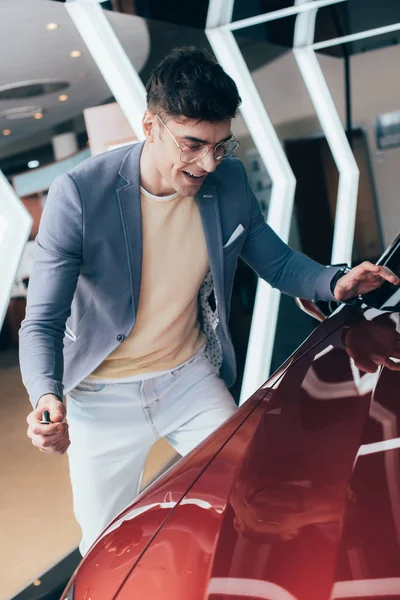 Excitado hombre con estilo en gafas mirando el automóvil rojo - foto de stock