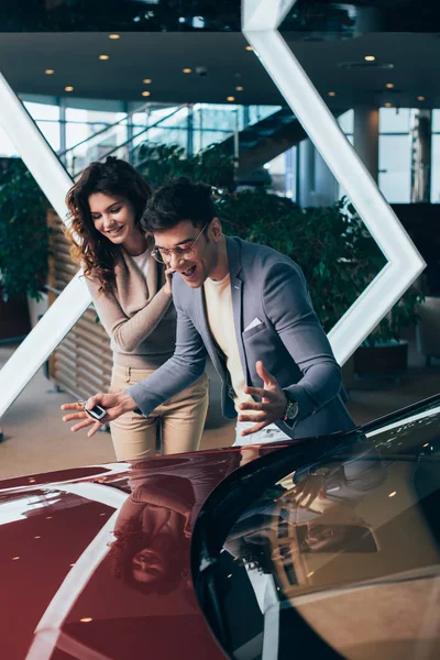 Excité homme geste tout en regardant voiture rouge avec fille bouclée heureuse — Photo de stock