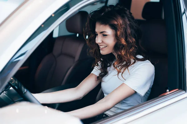 Messa a fuoco selettiva di donna riccia allegra seduta in automobile — Foto stock