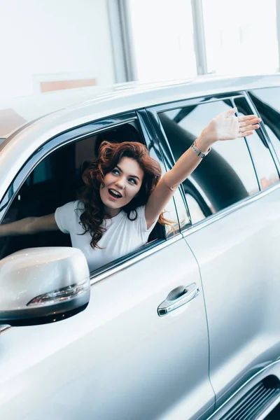 Selektiver Fokus einer aufgeregten, lockigen Frau, die schreit, während sie im Auto mit der Hand winkt — Stockfoto