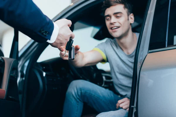 Vista cortada do negociante do carro que dá chaves ao homem bem sucedido que senta no carro — Fotografia de Stock