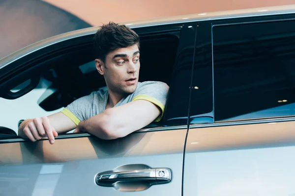 Selektiver Fokus eines überraschten gutaussehenden Mannes, der im Auto sitzt — Stockfoto