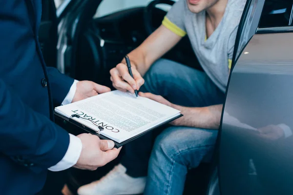 Geschnittene Ansicht von Autohändler hält Klemmbrett, während erfolgreicher Mann Vertrag unterzeichnet — Stockfoto