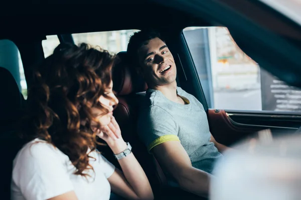 Messa a fuoco selettiva di uomo allegro guardando la donna riccia mentre seduto in automobile — Foto stock