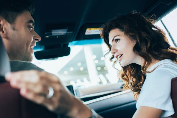 Selective focus of happy woman looking at handsome man while sitting in automobile — Stock Photo