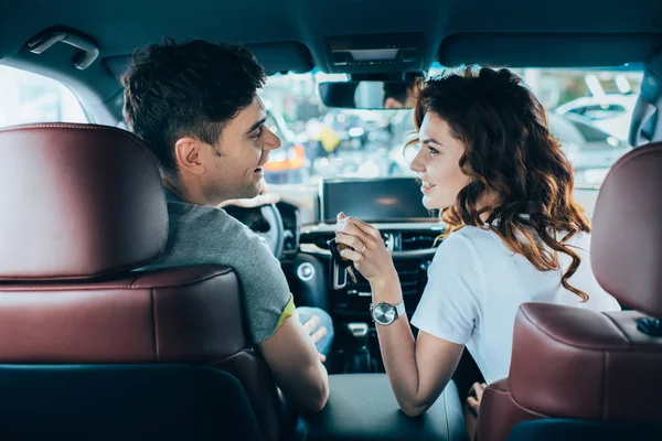 Selective focus of happy woman and handsome man looking at each other while sitting in automobile — Stock Photo