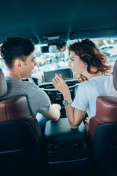 Selective focus of curly woman and handsome man looking at each other while sitting in automobile — Stock Photo