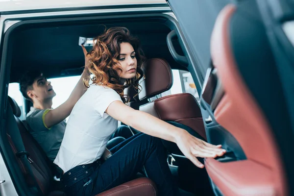 Foco seletivo de mulher encaracolado atraente fechando a porta do carro perto do homem enquanto sentado no automóvel — Fotografia de Stock