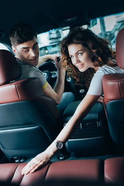 Selective focus of attractive curly woman sitting near happy man in automobile — Stock Photo