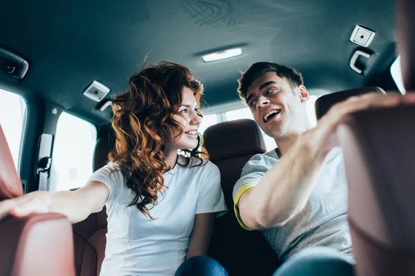 Selective focus of attractive curly woman looking at handsome man in automobile — Stock Photo