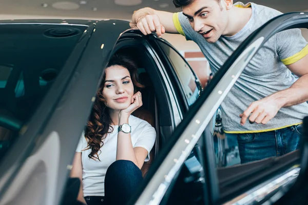 Selective focus of handsome man standing near attractive woman sitting in automobile — Stock Photo