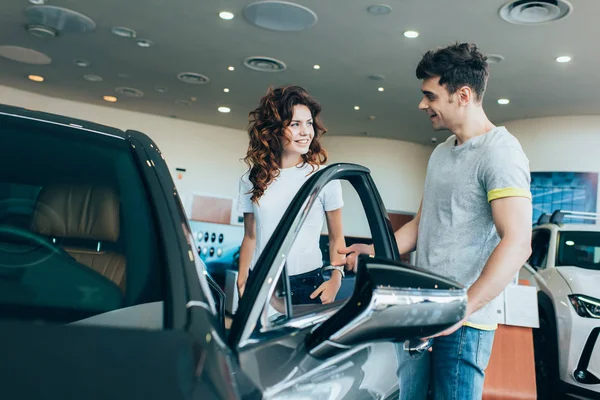 Selective focus of handsome man looking at attractive woman while opening car door — Stock Photo