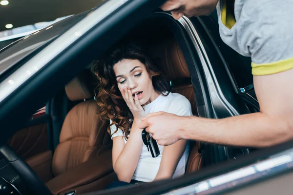 Enfoque selectivo del hombre guapo dando las llaves a la mujer sorprendida sentada en automóvil - foto de stock