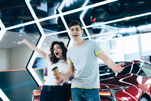 Cheerful man holding paper cup near curly woman while standing with outstretched hands — Stock Photo