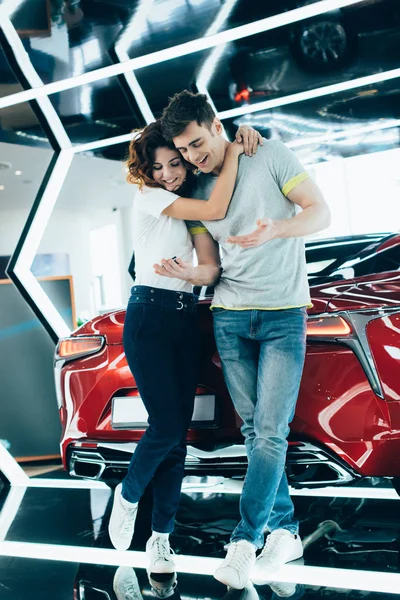 Весела кучерява жінка обіймає чоловіка, стоячи біля автомобіля — стокове фото