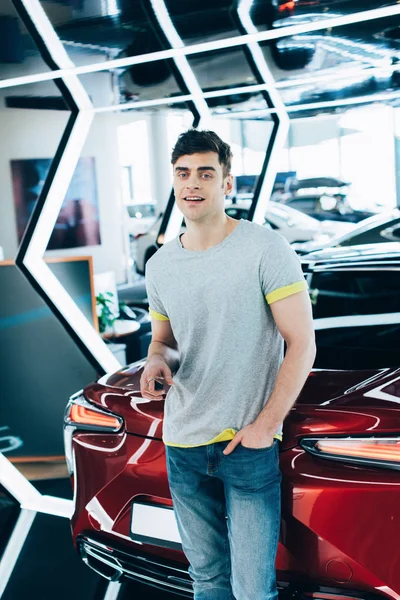 Fröhlicher Mann steht mit der Hand in der Tasche neben rotem Auto — Stockfoto