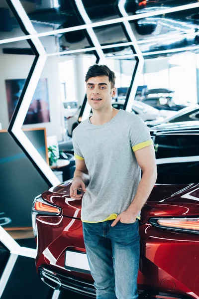 Cheerful man standing with hand in pocket near red car — Stock Photo