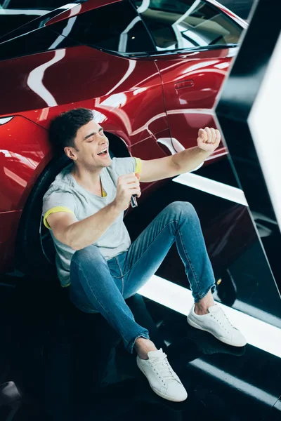 Selective focus of happy man sitting on floor with closed eyes near new car and celebrating triumph — Stock Photo